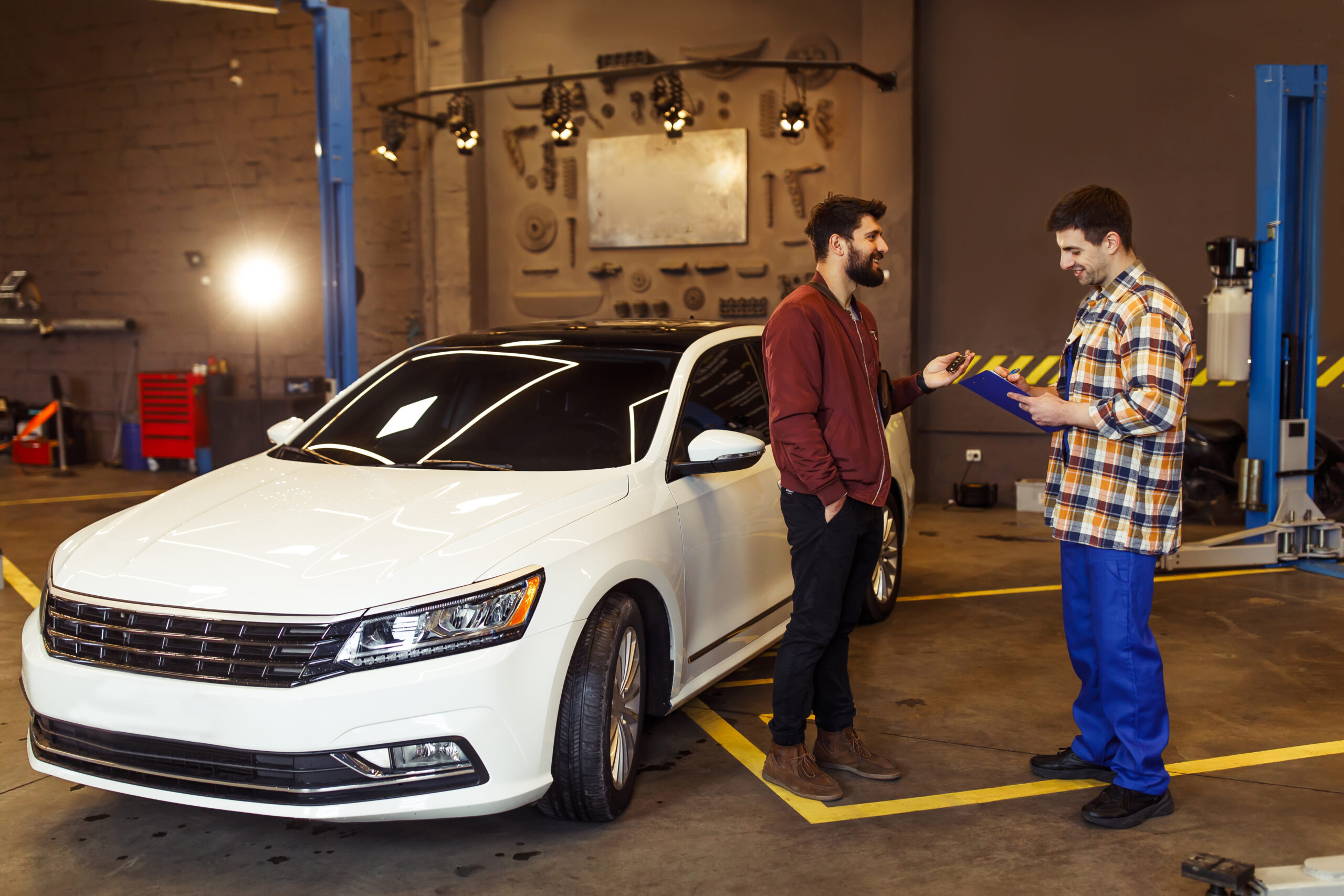male customer in auto service center explaning the problems of his car to mechanic with clipboard, sun effect